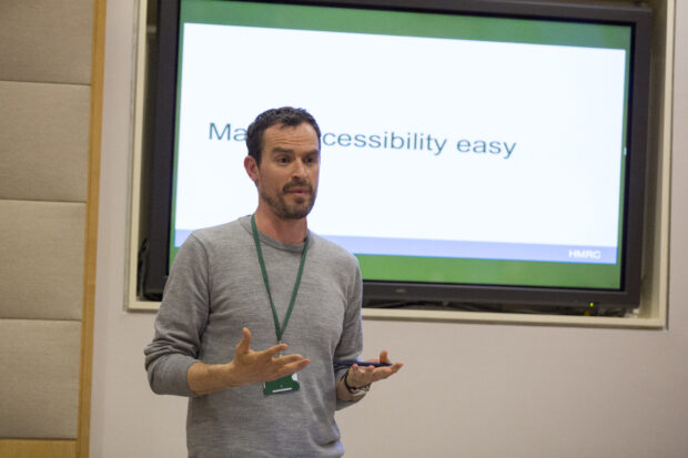 Alistair Duggin, Head of Accessibility at GDS, standing in front of a screen with the text 'Making accessibility easy'